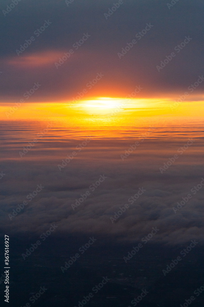 Hight shot from airplane of sun setting above fluffy clouds
