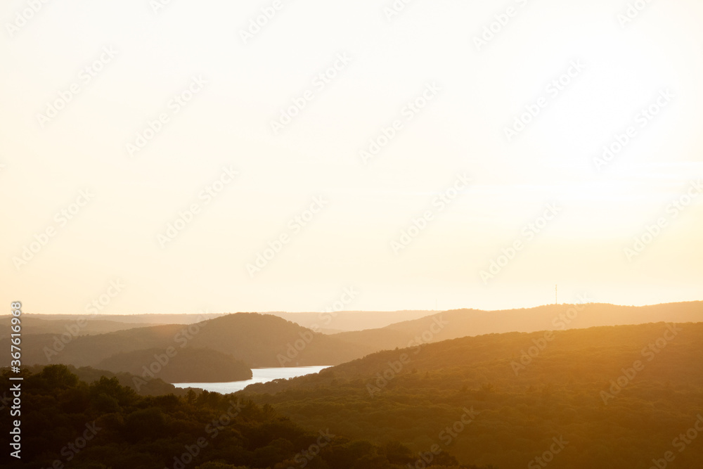 High view of the sun setting over a small lake and rolling hills