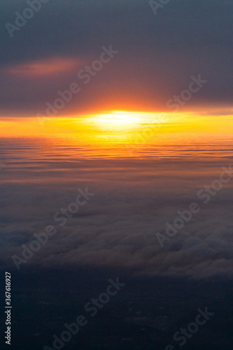 Hight shot from airplane of sun setting above fluffy clouds 