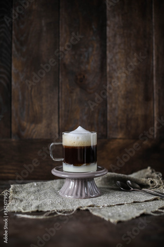 Cup of coffee on wooden table. Barraquito coffee in a small transparent cup on a ceramic stand. Dark brown wooden background. Drink in layers. photo