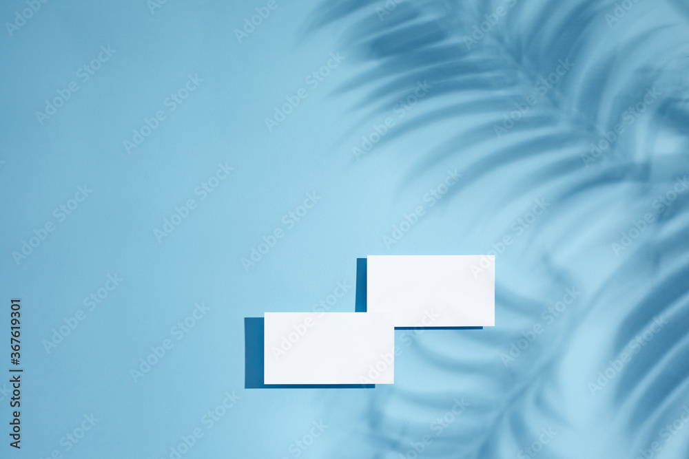 White empty blank business cards mockup with palm shadows on blue background. top view. stylish greeting card or wedding invitation White empty blank business cards mockup with palm shadows on blue background. top view. stylish greeting card or wedding invitation