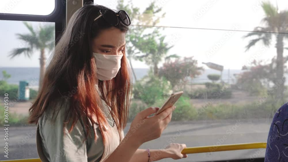Attractive young woman with smartphone wearing face protective medical mask for protection from virus disease sitting in bus Attractive young woman with smartphone wearing face protective medical mask for protection from virus disease sitting in bus