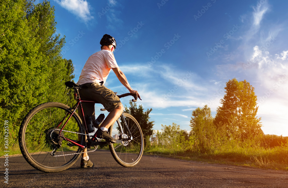 Cyclist with bicycle stands on the road at sunset. Man with road bike on the road against the blue sky.