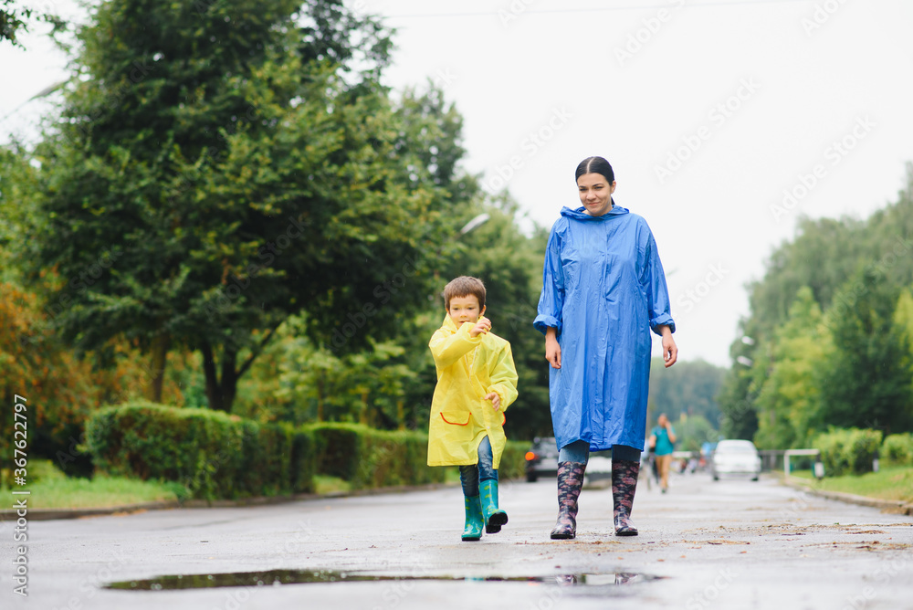 Fototapeta premium Mother and child, boy, playing in the rain, wearing boots and raincoats