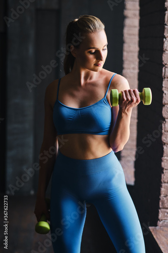 athletic young woman doing a sport fitness workout with dumbbells at gym