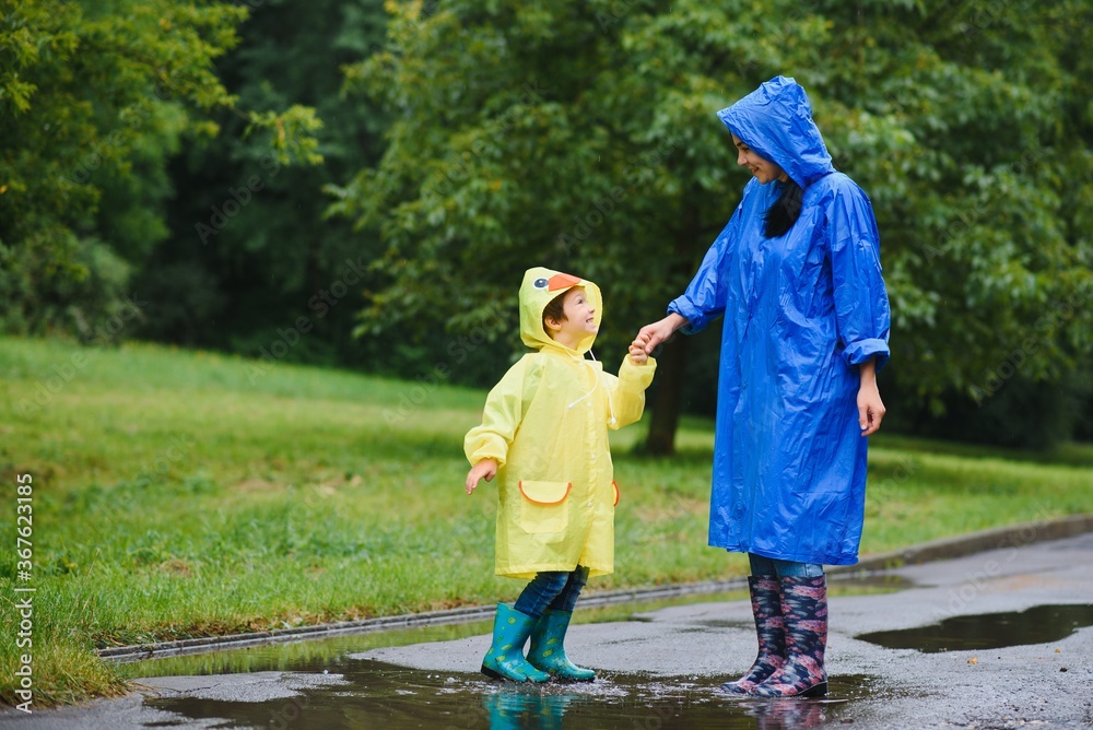 Fototapeta premium Mom and son in raincoats have fun together in the rain. concept of family vacation and happy childhood.