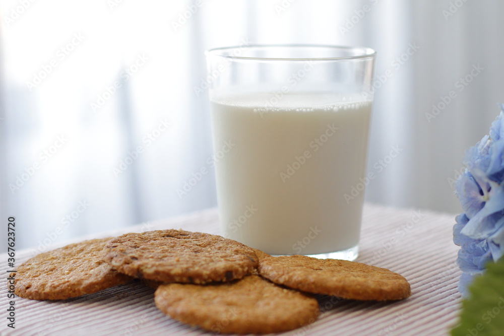 Oat cookies with glass of milk for breakfast on table cloth and blue flower on background, rustic healthy food Oat cookies with glass of milk for breakfast on table cloth and blue flower on background, rustic healthy food