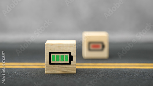 cube with full charged battery symbol and a cube out of focus with low energy symbol on asphalt surface