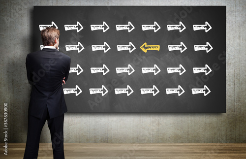 businessman looking at a chalkboard with an arrow symbol that is different from all others photo