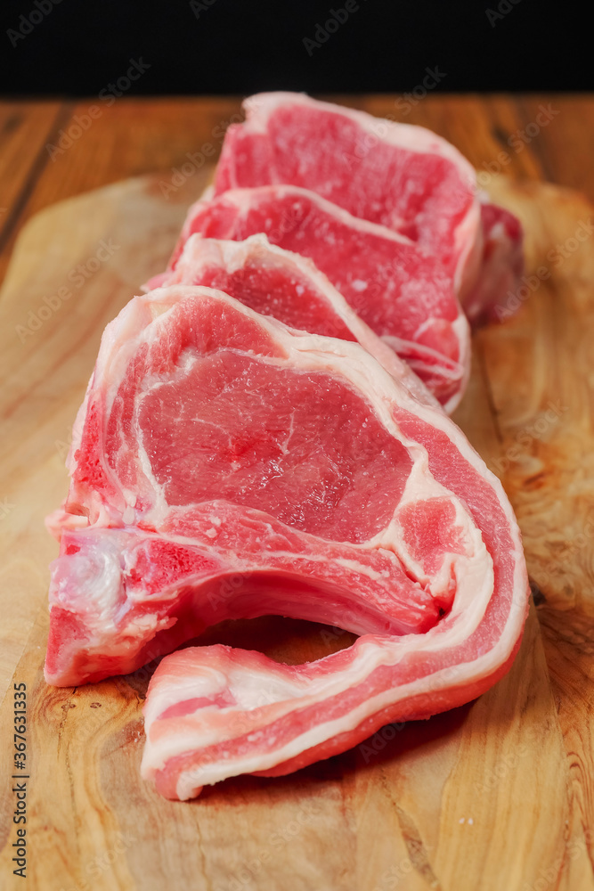 Fresh uncooked lamb loin chops on a wooden board, black background, Close up, Butcher craft concept. Vertical shot. Fresh uncooked lamb loin chops on a wooden board, black background, Close up, Butcher craft concept. Vertical shot.