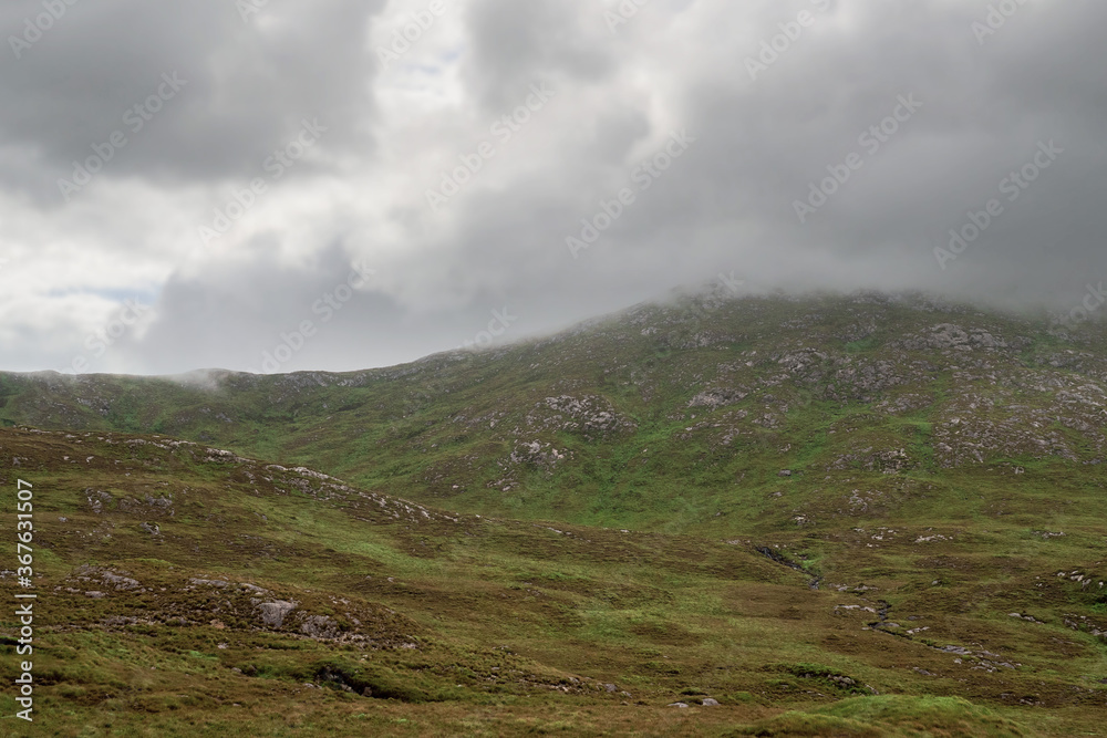 Mountains peaks in clouds, Connemara region, West of Ireland.  Rough terrain with green grass. Cloudy moody sky.