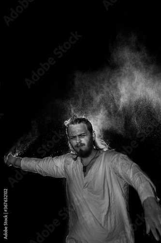 A man in white flax costume and colored smoke. Dark background