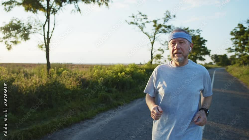 Blonde adult bearded man running using smart watch tapping touchscreen enjoying healthy active lifestyle. Male runner working out cardio exercise on summer sunset. Portable modern earphones. 4K Blonde adult bearded man running using smart watch tapping touchscreen enjoying healthy active lifestyle. Male runner working out cardio exercise on summer sunset. Portable modern earphones. 4K