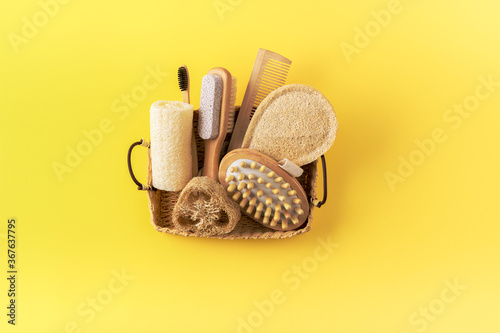 Anti cellulite massager, bamboo toothbrush, loofah sponge, wooden comb, peeling brush in basket on yellow. Eco friendly bathroom accessories. Zero waste concept. Minimalistic style. Copy space.