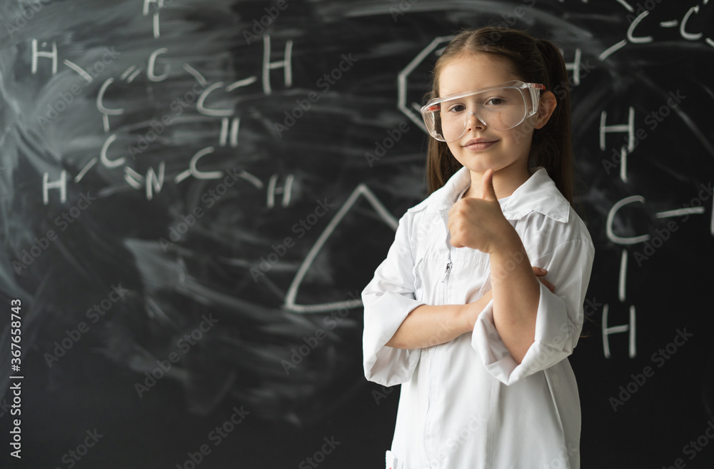 Schoolgirl girl stands near the chalkboard with formulas. Raises the thumb up.