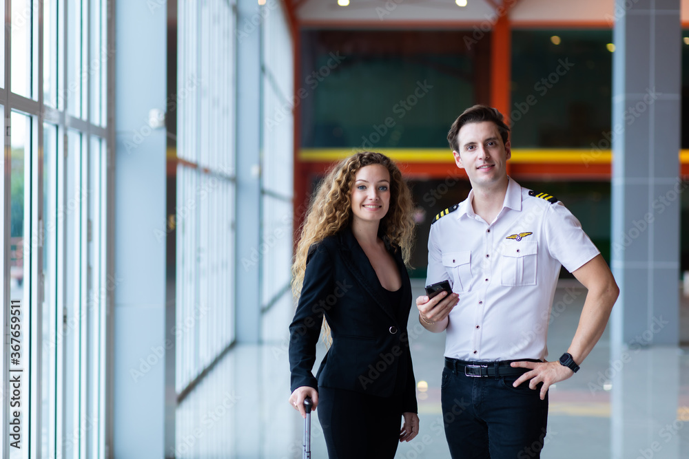 Young handsome man pilot in uniform standing at airport with beautiful young business woman