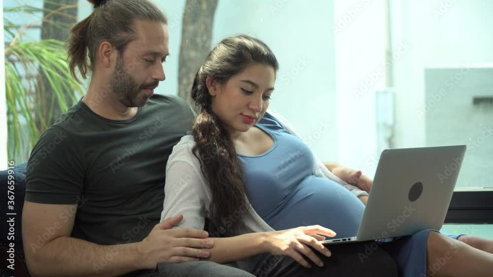 pregnant woman sitting on sofa with husband Using Laptop Computer Together in living room at home. Couple in love concept pregnant woman sitting on sofa with husband Using Laptop Computer Together in living room at home. Couple in love concept