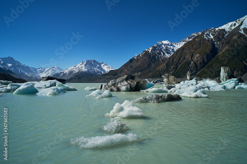 Scenic view overlooking a beautiful glacier river lake filled with melting floating icebergs surrounded by rocky landscape with snow covered mountain peaks in the background in Mt Cook New Zealand. photo