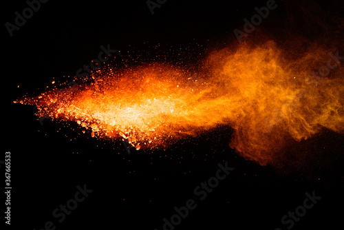Freeze motion of orange color powder exploding on black background. 