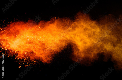 Freeze motion of orange color powder exploding on black background. 