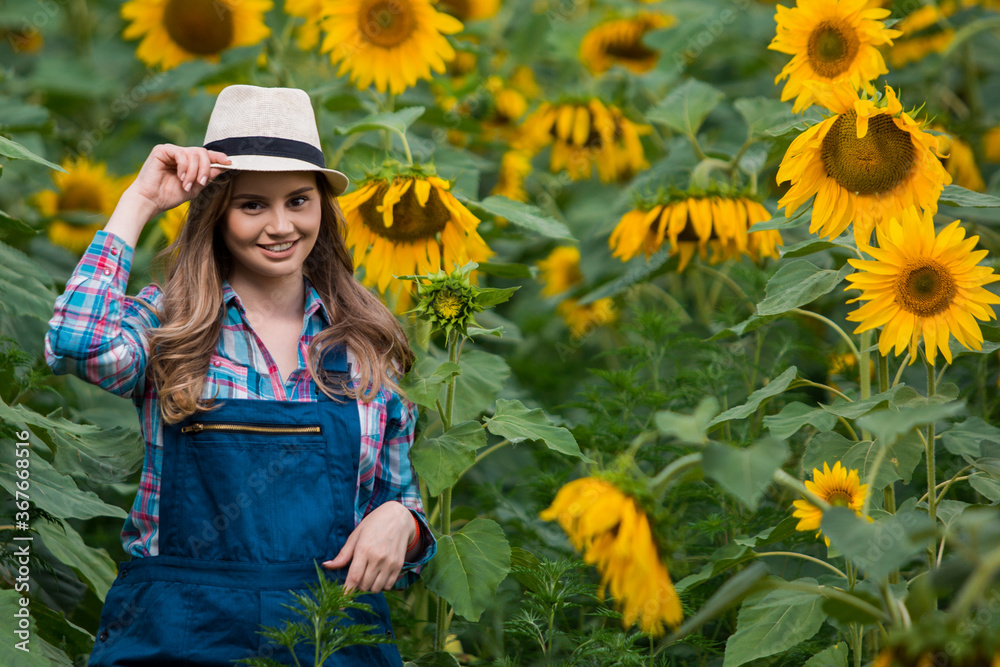 Gorgeous, young, energetic, female farmer walking through a beautiful golden and green sunflower field.