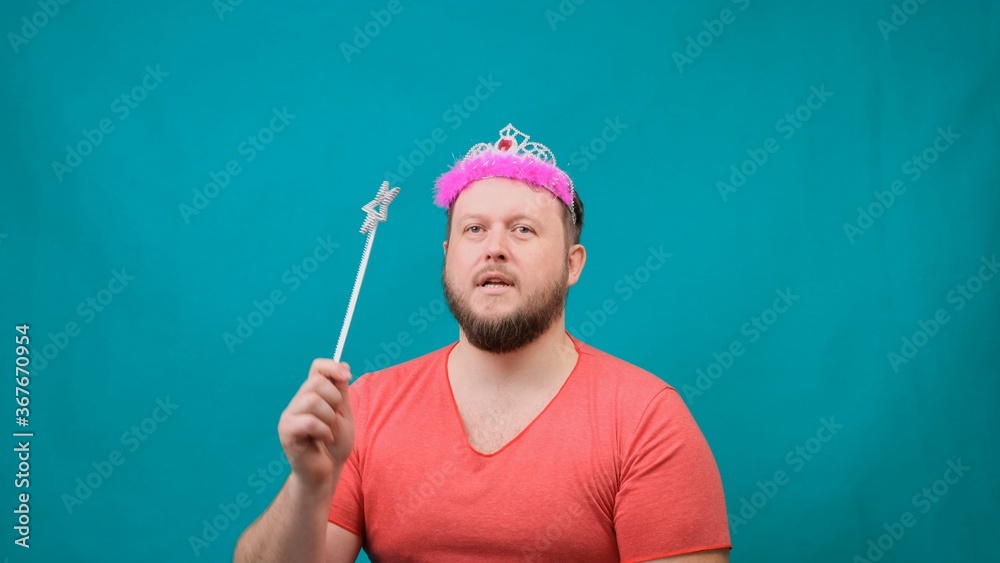 funny bearded freaky man in a pink T-shirt with a deadema on his head is dreaming with a magic wand in his hand. A funny wizard joke to make and fulfill a wish. funny bearded freaky man in a pink T-shirt with a deadema on his head is dreaming with a magic wand in his hand. A funny wizard joke to make and fulfill a wish.