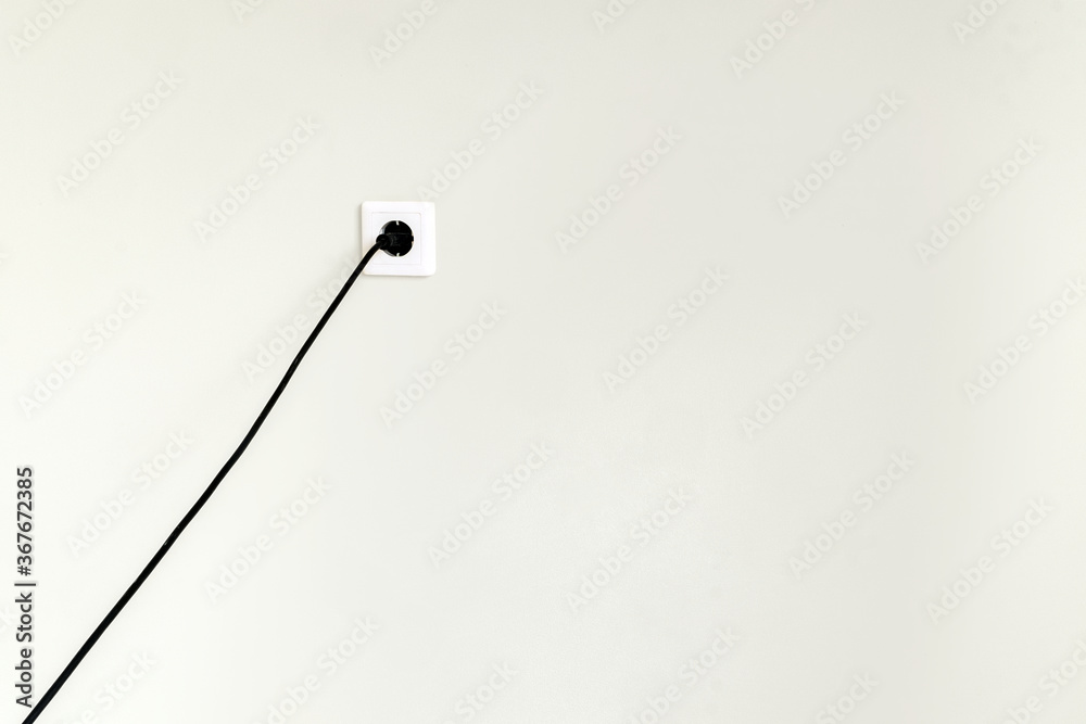 White electrical outlet with black wire and plug on a white wall in a city apartment. White electrical outlet with black wire and plug on a white wall in a city apartment.