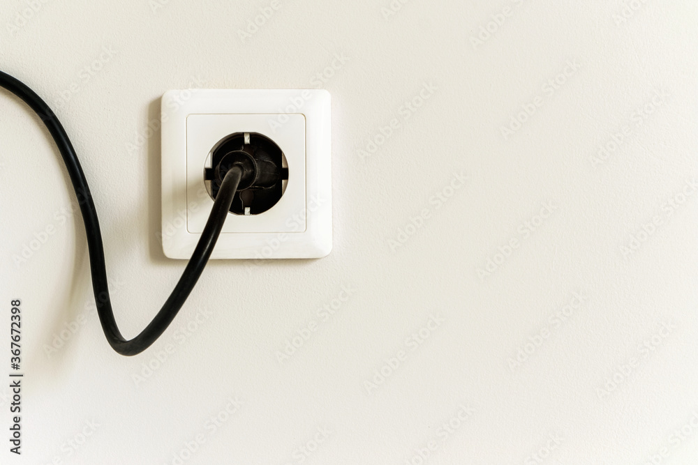 White electrical outlet with black wire and plug on a white wall in a city apartment. White electrical outlet with black wire and plug on a white wall in a city apartment.