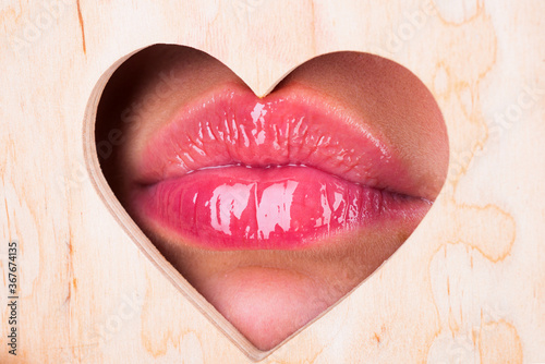 Heart shape. Girl Natural beauty lips. Red lip with glossy lipgloss. Close up, macro with beautiful mouths. Sexy kiss, sensual seductive lips of a young woman. Cosmetics and beauty salon.