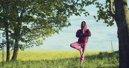 Front view of young woman practicing yoga outdoors on nature background slow motion. Female yogi girl standing in tree pose vriksasana in countryside copy text space. Healthy body lifestyle concept photo