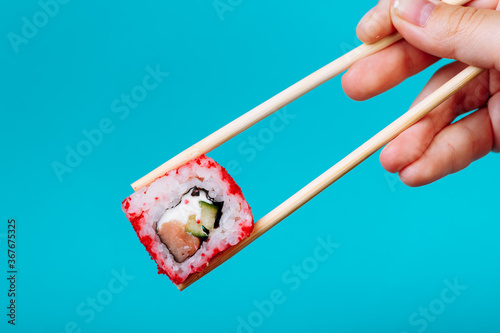 Tasty califiornia roll with wooden chopsticks on blue background close up. Place for caption and text
