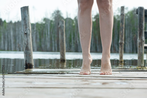 Female feet on the old pier on lake water background. Countryside vacation background.