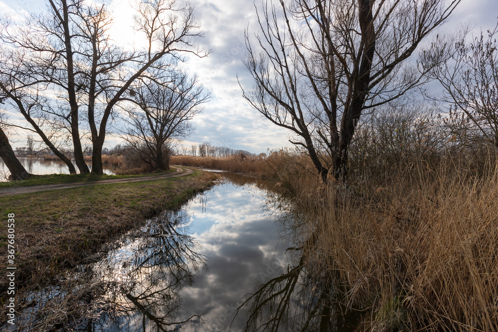 Water channel through which the bridge leads. around are ponds and mature trees. In the background is a blue sky with clouds. Water channel through which the bridge leads. around are ponds and mature trees. In the background is a blue sky with clouds.