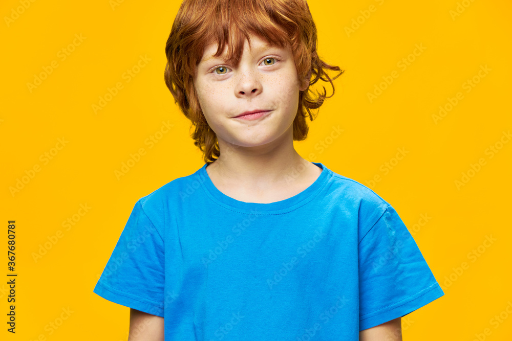 Close-up of a handsome boy looking ahead blue t-shirt yellow background red hair Close-up of a handsome boy looking ahead blue t-shirt yellow background red hair
