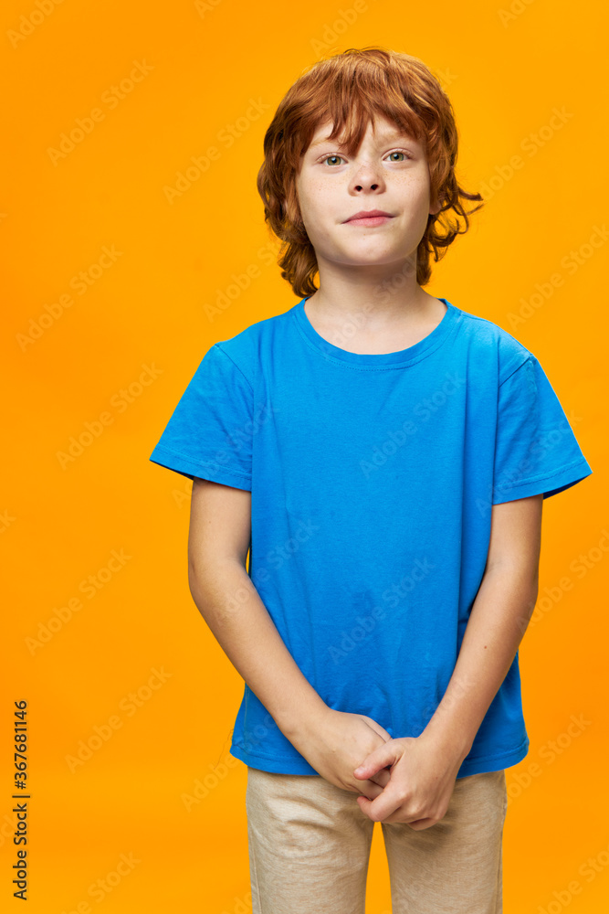 redhead boy has joined hands and is looking straight blue t-shirt yellow background redhead boy has joined hands and is looking straight blue t-shirt yellow background