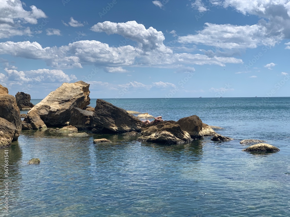 Background texture: large stones of various shapes in the sea. A pile of granite boulders against the background of the sea and sky. Rock destroyed by the waves. Concept - stone, hardness