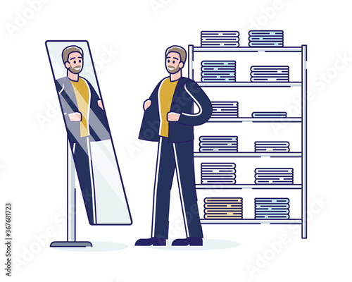 Man on shopping trying suit looking on mirror reflection in dressing room of fashionable boutique