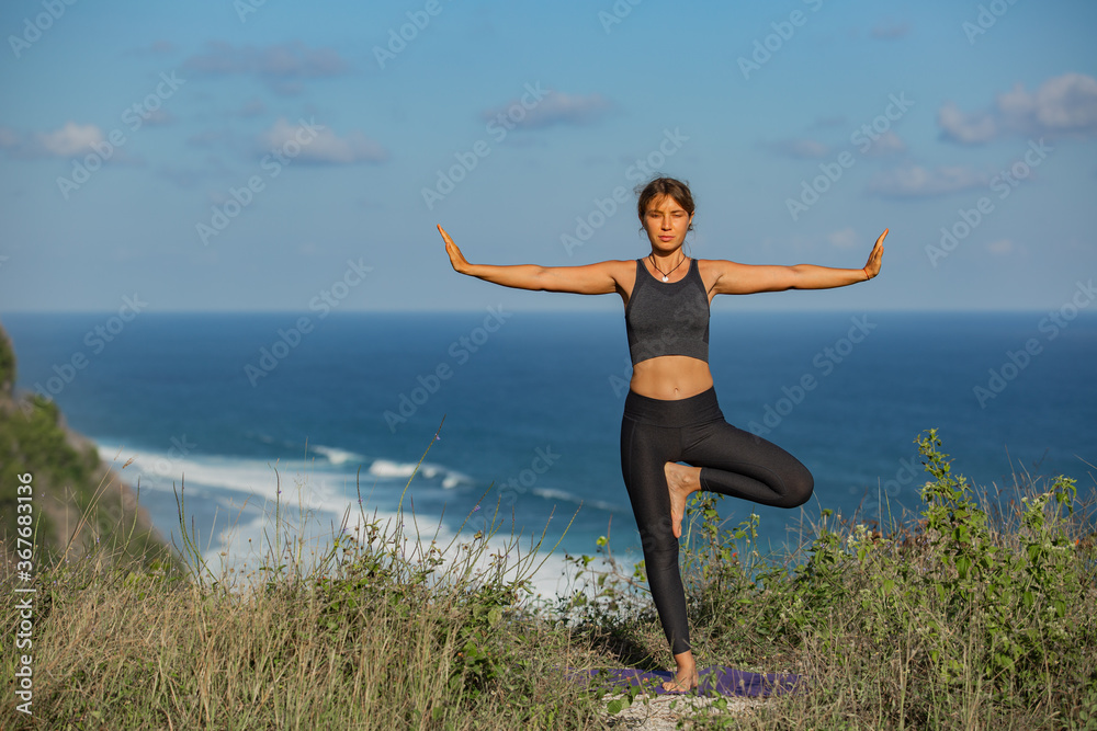 Young woman doing yoga outdoors with amazing back view. Bali. Indonesia.