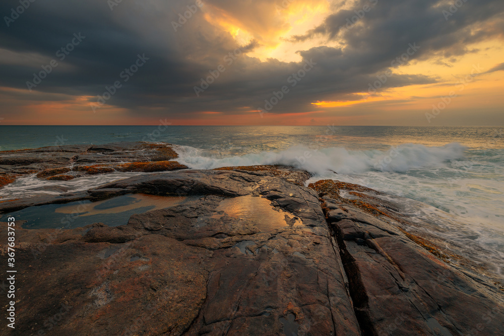 Fototapeta premium Rocks and stones at the ocean coast under a beautiful sunset sky with clouds on Sri Lanka island.