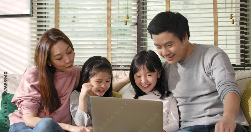 Happy asian family parents and little children enjoy using devices together sit on sofa, technology addicted couple with kids having fun with laptop computer at home. Social distancing self isolation.