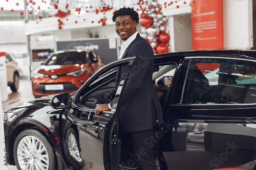 Man buying the car. Businessman in a car salon. Black male in a suit. © prostooleh