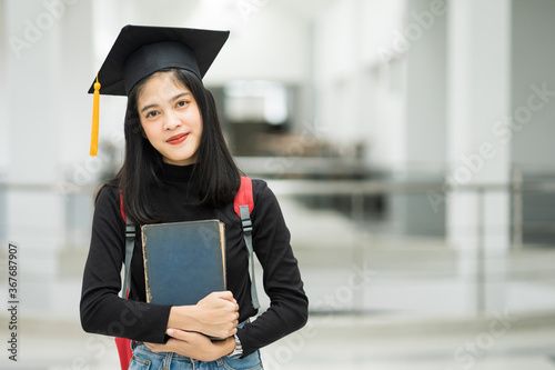 Portrait of female teenager college student holding books with school backpack and wearing graduation hat represent graduation concept.