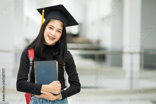 Portrait of female teenager college student holding books with school backpack and wearing graduation hat represent graduation concept.