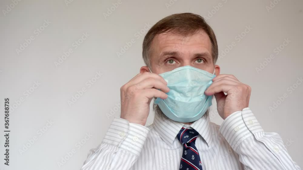 Adult man in white shirt and tie puts on medical mask and sighs. Prevention of infection. Adult man in white shirt and tie puts on medical mask and sighs. Prevention of infection.