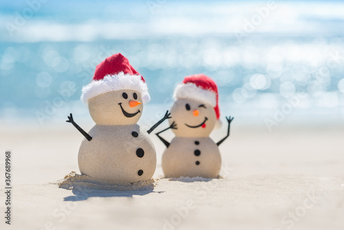 Two Sandy Christmas Snowmen are celebrating Christmas on a beautiful beach with beautiful bokeh in the background, one of them is only in focus