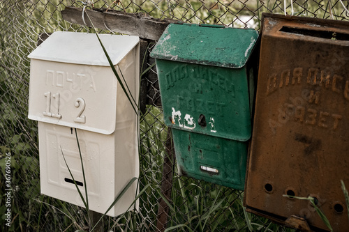Vintage rustic mailboxes of different colors pinned on a fence.