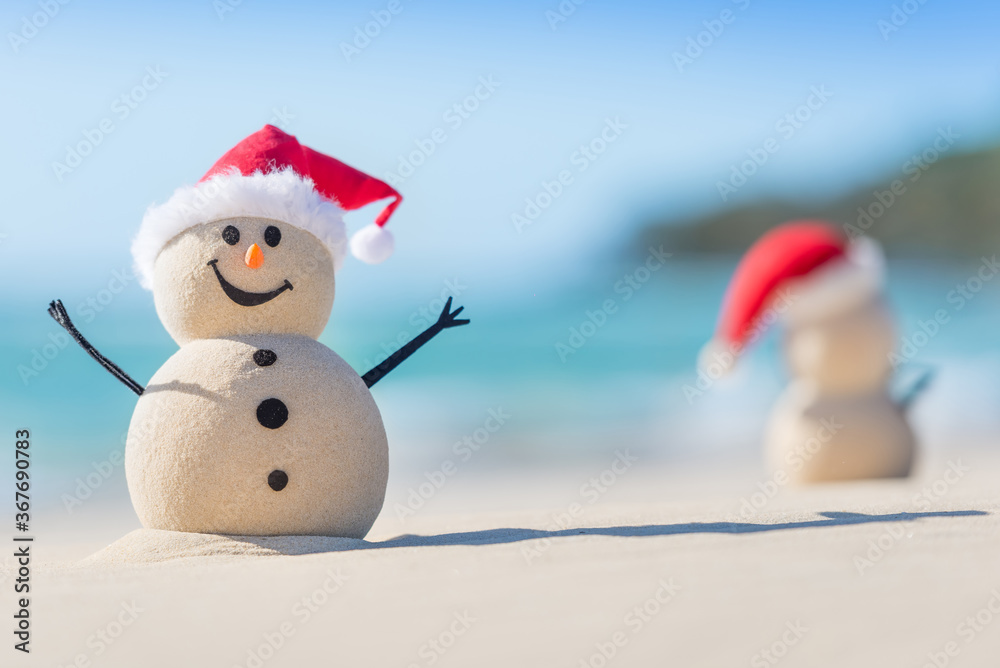 Two Sandy Christmas Snowmen are celebrating Christmas on a beautiful beach, one of them is out of focus and only shows it's back Two Sandy Christmas Snowmen are celebrating Christmas on a beautiful beach, one of them is out of focus and only shows it's back