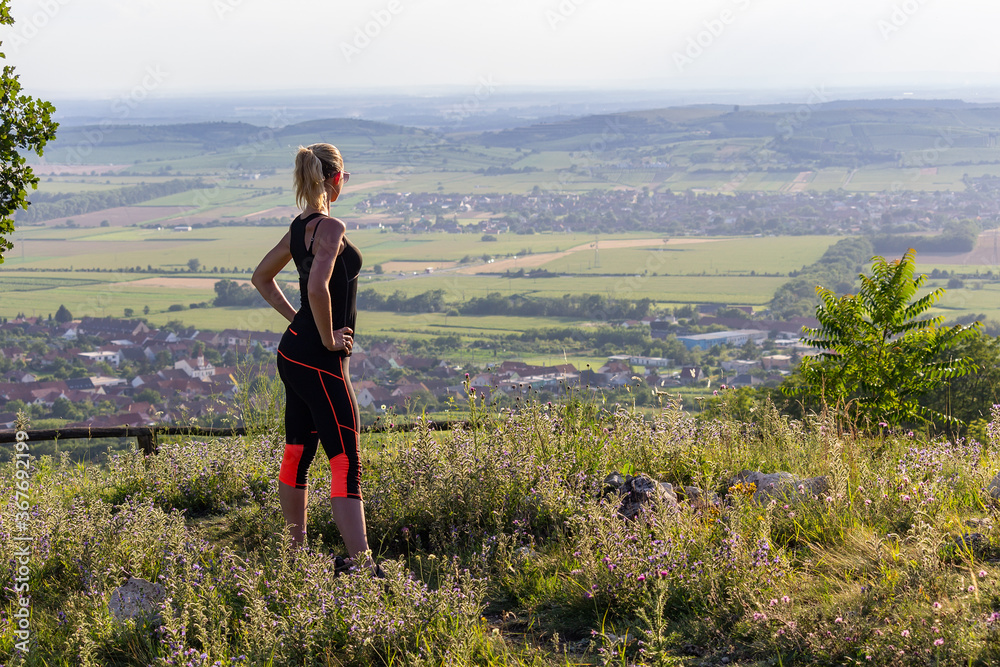 Young woman standing on lookout in fitness outfit and sunglasses looking to valley. Palava, Czech republic