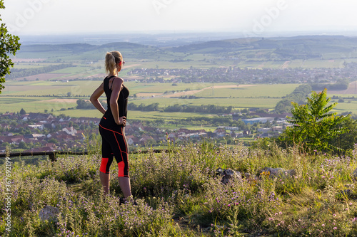 Young woman standing on lookout in fitness outfit and sunglasses looking to valley. Palava, Czech republic © Space Creator