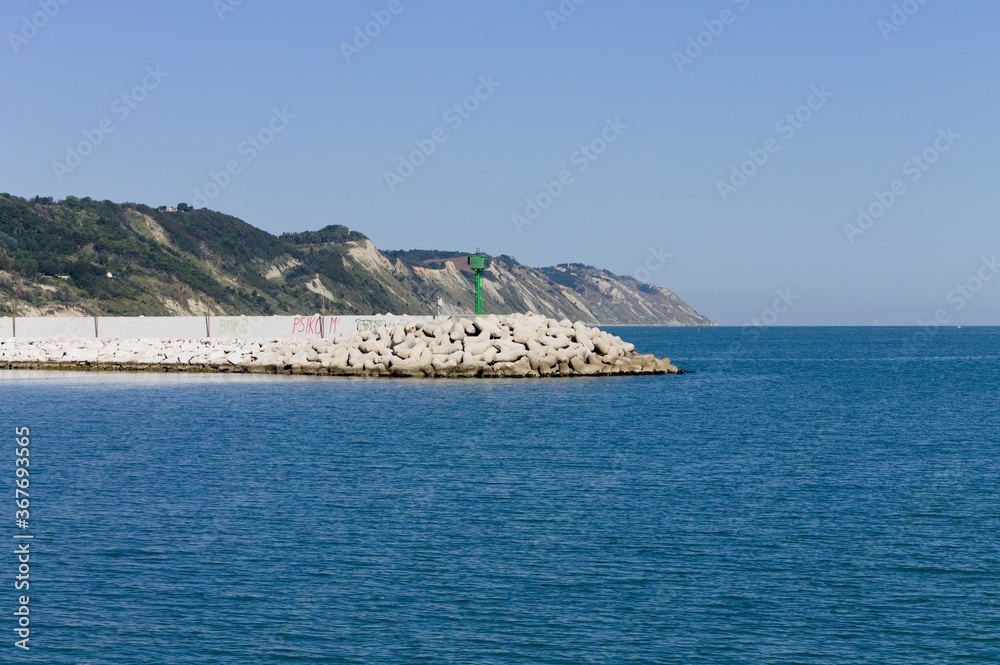 The pier of Pesaro harbor with breakwater tetrapods and a small green lighthouse (Pesaro, Italy, Europe)